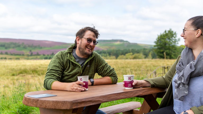 Visitors sat at a picnic table enjoying a drink outside the Longshaw Café at Longshaw, Burbage and the Eastern Moors, Derbyshire